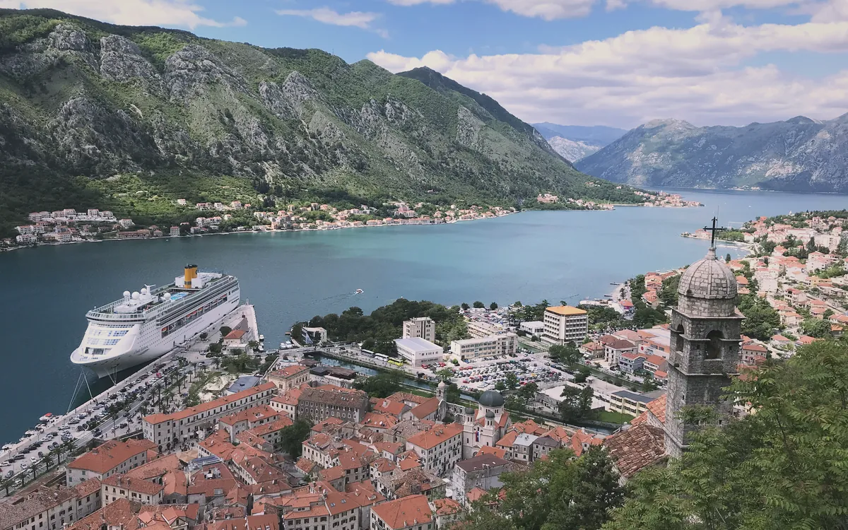 Kotor Körfezi'nde dağlarla çevrili tarihi şehir ve limana demirlemiş büyük bir yolcu gemisi.