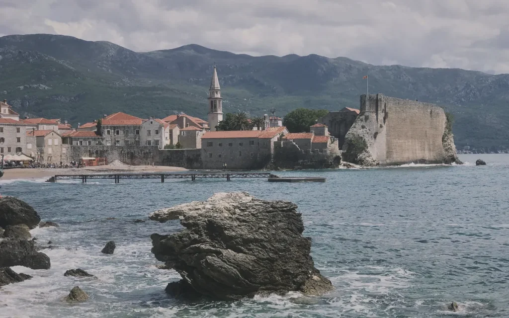 Karadağ'ın Budva Eski Şehir'i, tarihi surları, çan kulesi ve denizi gösteren geniş bir manzara.