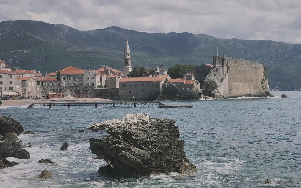 Karadağ'ın Budva Eski Şehir'i, tarihi surları, çan kulesi ve denizi gösteren geniş bir manzara.